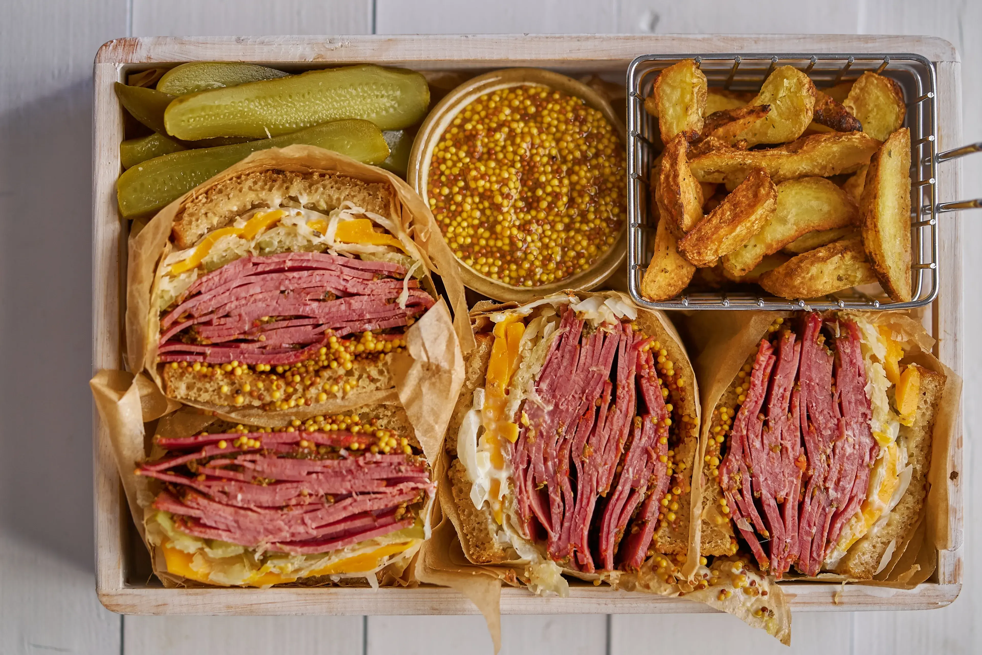 Enormous sandwiches with pastrami beef in wooden box. Served with baked potatoes, pickles Enormous sandwiches with pastrami beef in wooden box. Served with baked potatoes, pickles